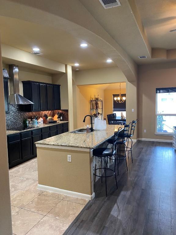 kitchen featuring a kitchen bar, light stone counters, backsplash, arched walkways, and wall chimney exhaust hood