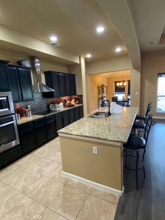 kitchen with arched walkways, a sink, a kitchen bar, stainless steel oven, and wall chimney range hood