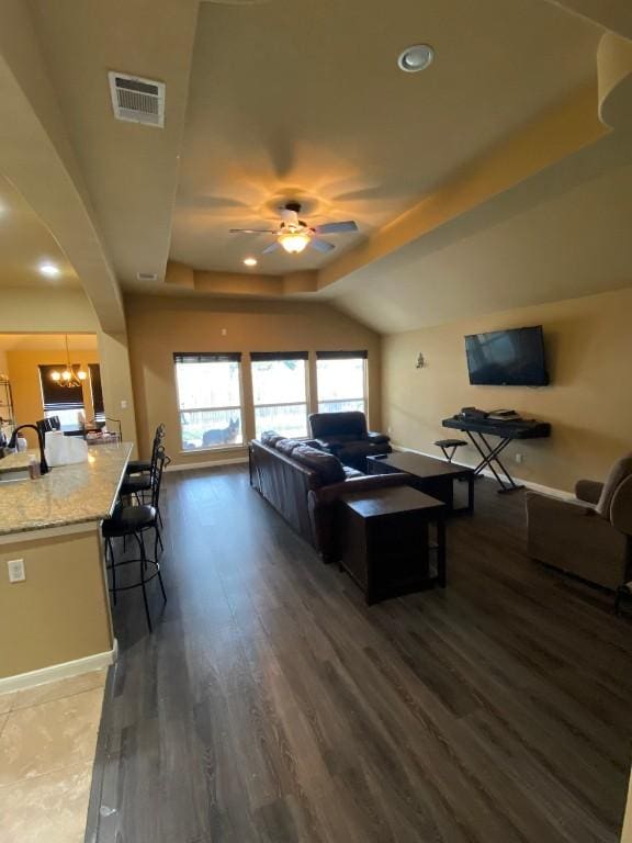 living area featuring wood finished floors, visible vents, lofted ceiling, arched walkways, and ceiling fan with notable chandelier