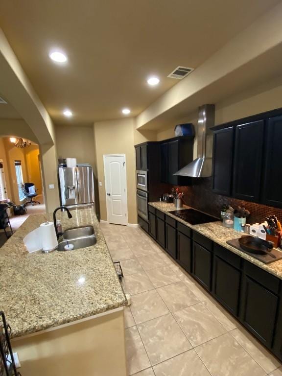 kitchen featuring visible vents, arched walkways, stainless steel fridge with ice dispenser, wall chimney range hood, and black electric cooktop