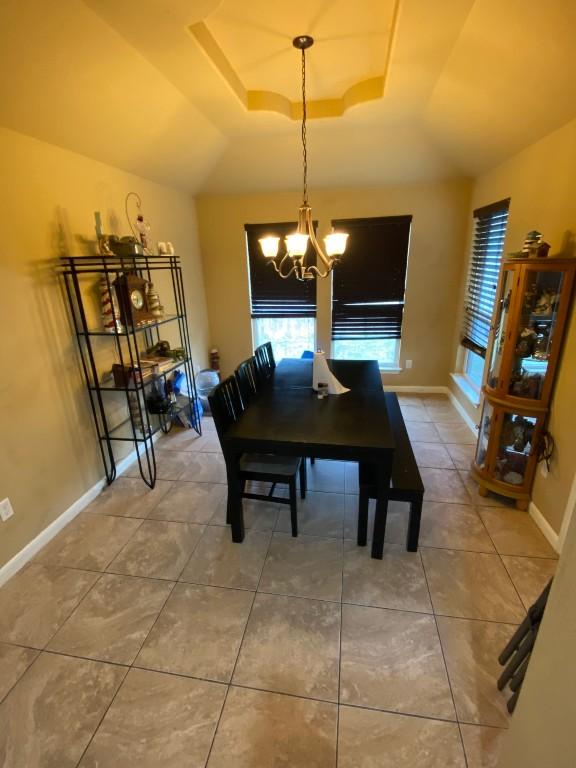 dining room with tile patterned floors, baseboards, a raised ceiling, and an inviting chandelier