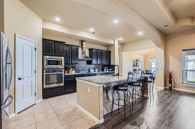 206 Swenson Dr, Hutto, TX 78634 - kitchen featuring appliances with stainless steel finishes, wall chimney exhaust hood, a kitchen breakfast bar, an island with sink, and backsplash
