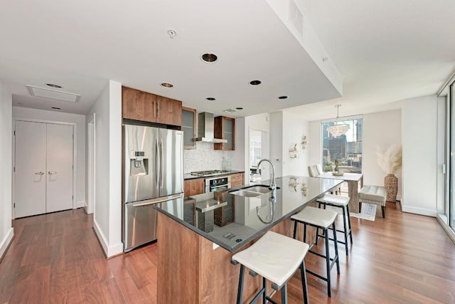 kitchen with stainless steel appliances, a sink, a kitchen breakfast bar, wall chimney range hood, and brown cabinets