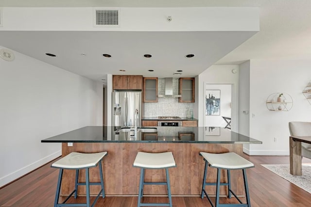 kitchen featuring dark countertops, visible vents, dark wood-type flooring, wall chimney range hood, and stainless steel fridge with ice dispenser