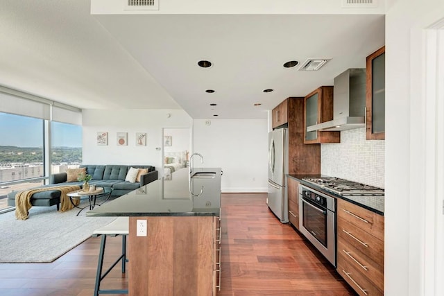 kitchen featuring dark countertops, wall chimney range hood, a kitchen bar, and stainless steel appliances