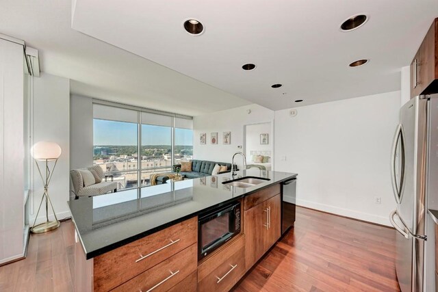 kitchen featuring black microwave, wood finished floors, a sink, freestanding refrigerator, and an island with sink