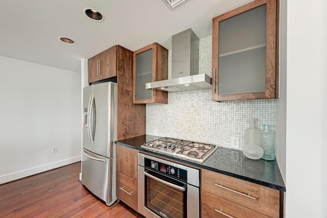 kitchen with appliances with stainless steel finishes, wall chimney range hood, backsplash, dark wood-style floors, and brown cabinetry