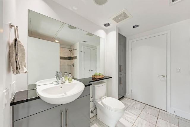 bathroom featuring toilet, tiled shower, vanity, and visible vents