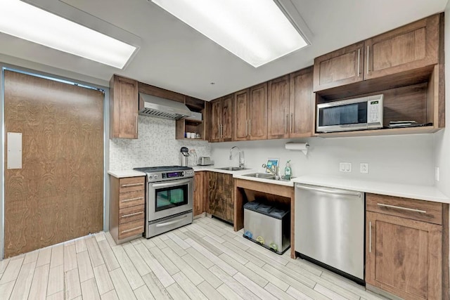 kitchen with stainless steel appliances, light countertops, backsplash, a sink, and wall chimney exhaust hood