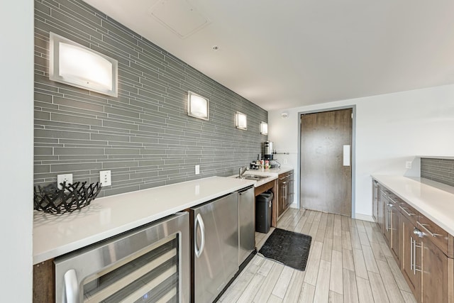 kitchen with wine cooler, light countertops, wood tiled floor, a sink, and fridge