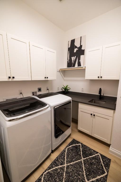 laundry area featuring light wood-type flooring, cabinet space, washer and dryer, and a sink