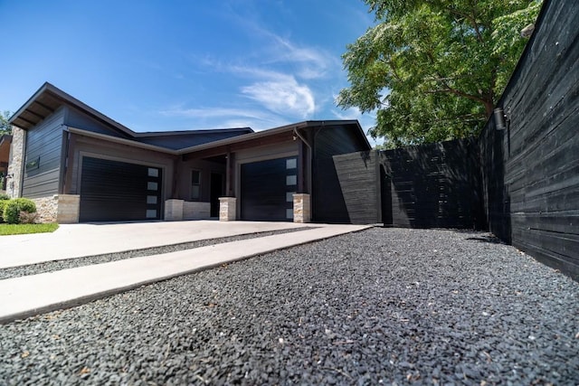 view of side of home with a garage, stone siding, fence, and gravel driveway