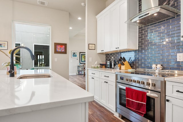 103 Hans Bell Dr, Blanco, TX 78606 - kitchen featuring stainless steel range oven, wall chimney range hood, dark wood finished floors, decorative backsplash, and white cabinets