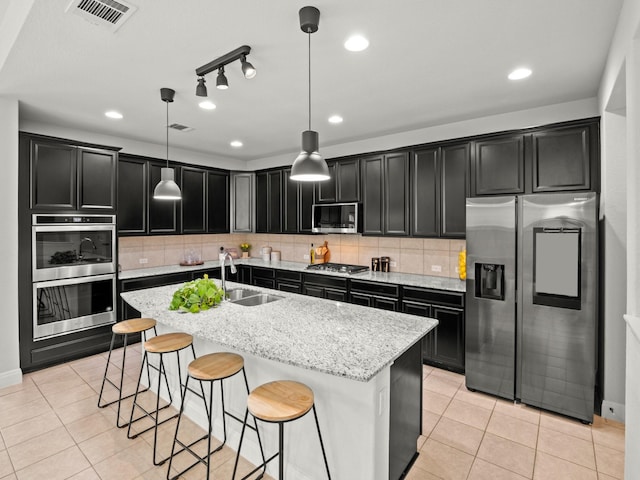 kitchen with appliances with stainless steel finishes, sink, hanging light fixtures, light stone countertops, and a center island with sink