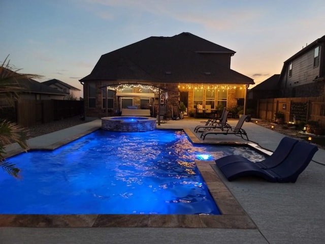 pool at dusk with a patio, an in ground hot tub, and pool water feature