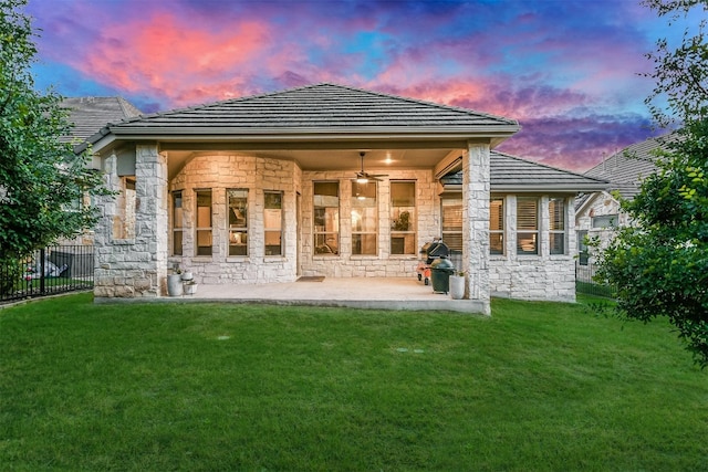 back of house with stone siding, a patio area, fence, and a yard