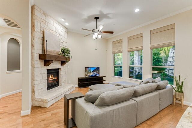 living room with crown molding, a stone fireplace, hardwood / wood-style flooring, and ceiling fan