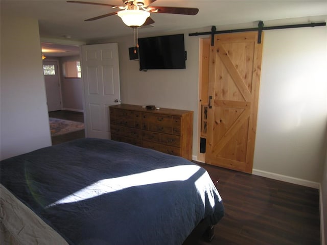 bedroom with a barn door, ceiling fan, and dark hardwood / wood-style floors