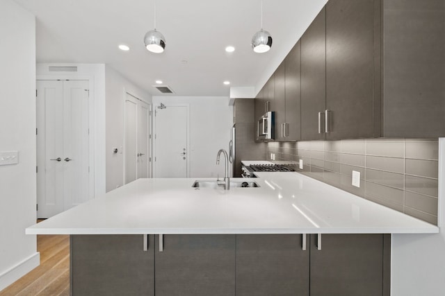 kitchen with appliances with stainless steel finishes, decorative light fixtures, light hardwood / wood-style floors, and a breakfast bar