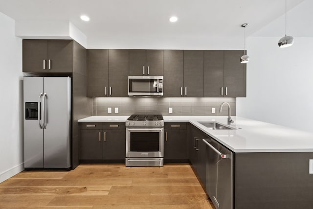 kitchen with sink, stainless steel appliances, tasteful backsplash, pendant lighting, and light wood-type flooring