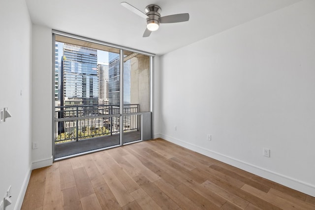 unfurnished room with ceiling fan, expansive windows, and light wood-type flooring