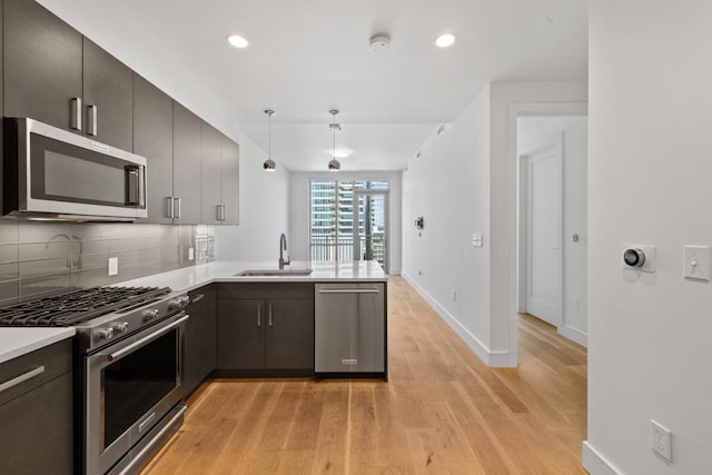 kitchen with sink, hanging light fixtures, stainless steel appliances, kitchen peninsula, and light wood-type flooring