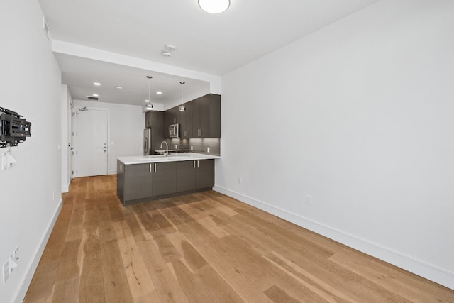 kitchen with stainless steel appliances, dark brown cabinetry, sink, and light hardwood / wood-style floors