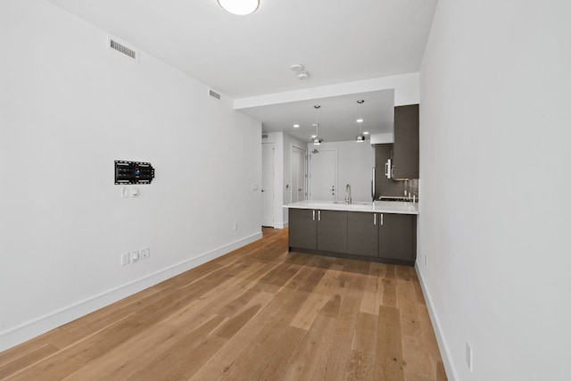 kitchen with light wood-type flooring, backsplash, hanging light fixtures, and sink