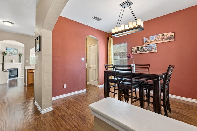 dining room featuring a fireplace, dark wood-type flooring, and a notable chandelier