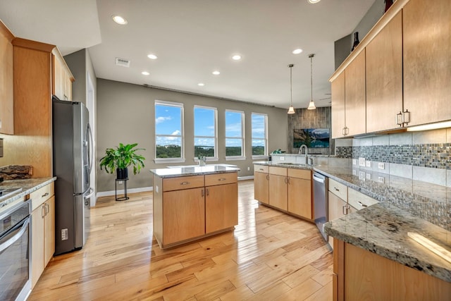 kitchen with decorative light fixtures, stainless steel appliances, light stone counters, a kitchen island, and light hardwood / wood-style floors