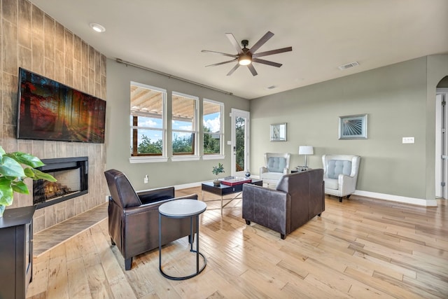 living room with light wood-type flooring, ceiling fan, and a tiled fireplace