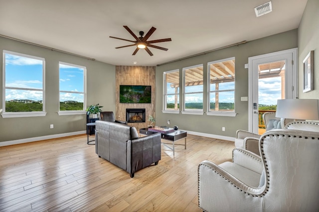 living room with a large fireplace, ceiling fan, light hardwood / wood-style floors, and a healthy amount of sunlight