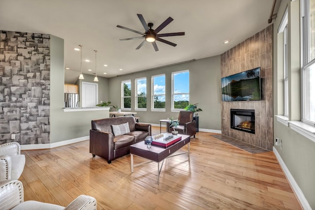 living room with light wood-type flooring, ceiling fan, and a tile fireplace