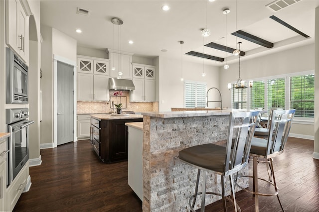 kitchen featuring a breakfast bar, white cabinetry, hanging light fixtures, appliances with stainless steel finishes, and an island with sink