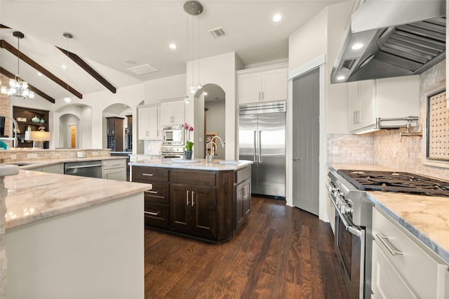 kitchen with wall chimney range hood, lofted ceiling with beams, a center island with sink, dark brown cabinets, and high quality appliances