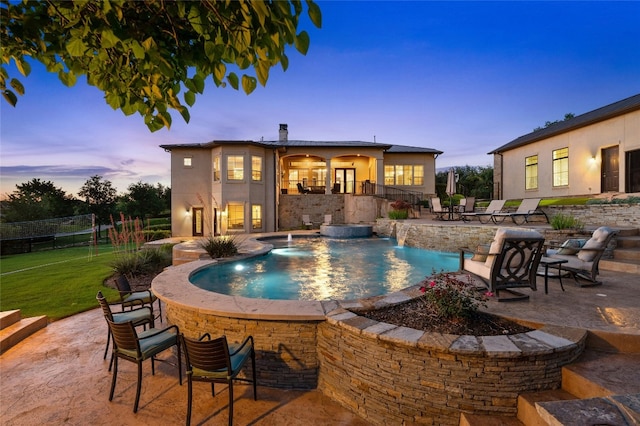 pool at dusk with pool water feature and a patio area