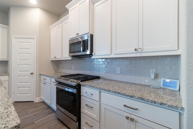 kitchen featuring light hardwood / wood-style flooring, appliances with stainless steel finishes, light stone counters, white cabinets, and decorative backsplash