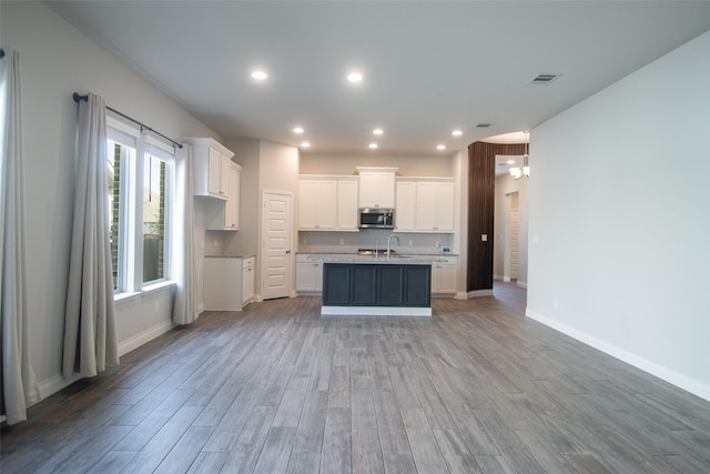 kitchen with white cabinetry, sink, an island with sink, and light wood-type flooring