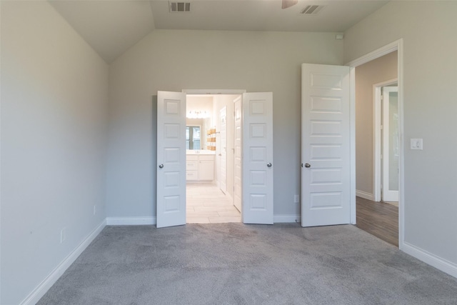 unfurnished bedroom featuring ensuite bathroom, vaulted ceiling, and light carpet