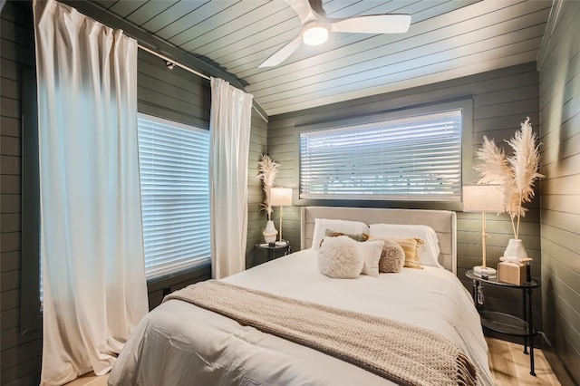 bedroom featuring wooden walls, wood finished floors, lofted ceiling, ceiling fan, and wood ceiling