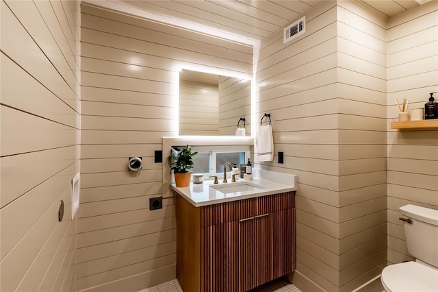 bathroom with visible vents, toilet, wood walls, and vanity