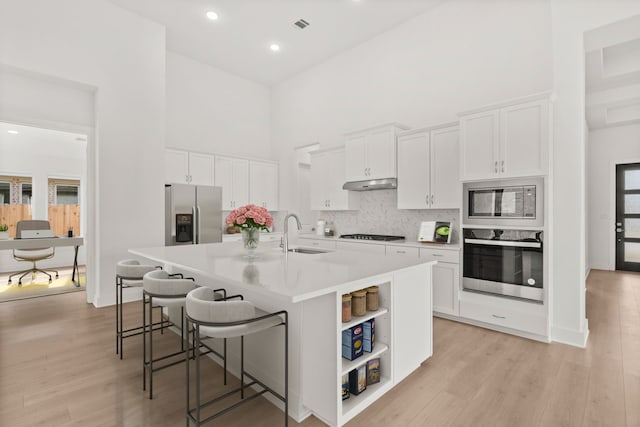 kitchen with a kitchen bar, a towering ceiling, a kitchen island with sink, appliances with stainless steel finishes, and white cabinets