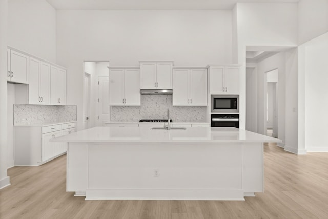 204 Camille St, Leander, TX 78641 - kitchen with a sink, wall oven, stainless steel microwave, a towering ceiling, and a kitchen island with sink
