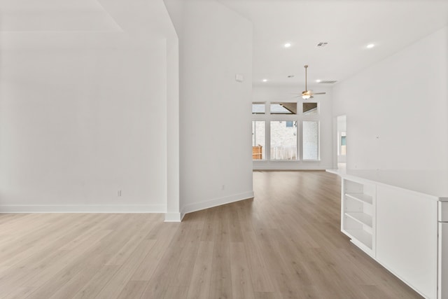 unfurnished room with ceiling fan, light wood-type flooring, and a high ceiling