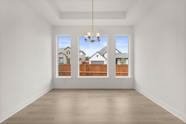 unfurnished dining area featuring light wood-type flooring, a tray ceiling, and a notable chandelier