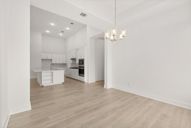 204 Camille St, Leander, TX 78641 - unfurnished living room with a sink, baseboards, a chandelier, light wood-style floors, and a towering ceiling