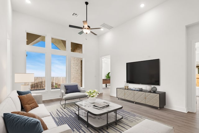 living room featuring ceiling fan, a towering ceiling, and hardwood / wood-style flooring