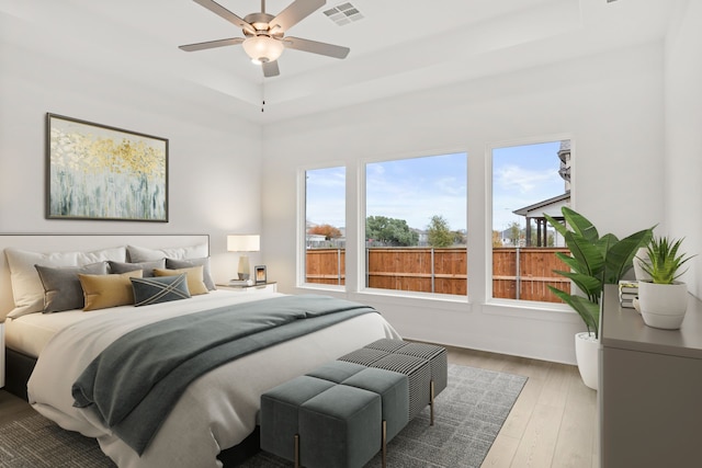 bedroom with ceiling fan, wood-type flooring, and a tray ceiling