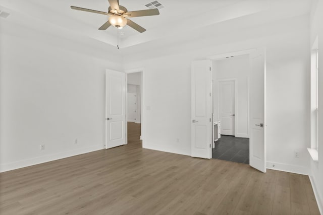 unfurnished bedroom with ceiling fan, a raised ceiling, and dark hardwood / wood-style floors