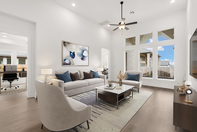 living room with ceiling fan, a towering ceiling, and wood-type flooring